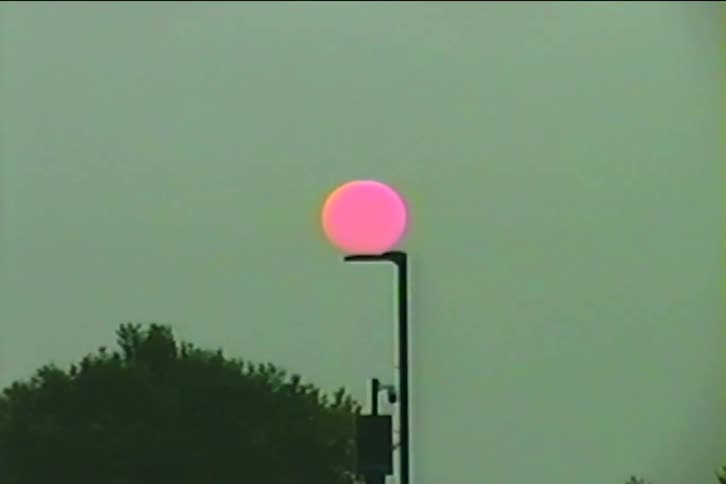 Vintage VHS footage captures a surreal pink sun appearing to rest on top of a street lamp at dusk
