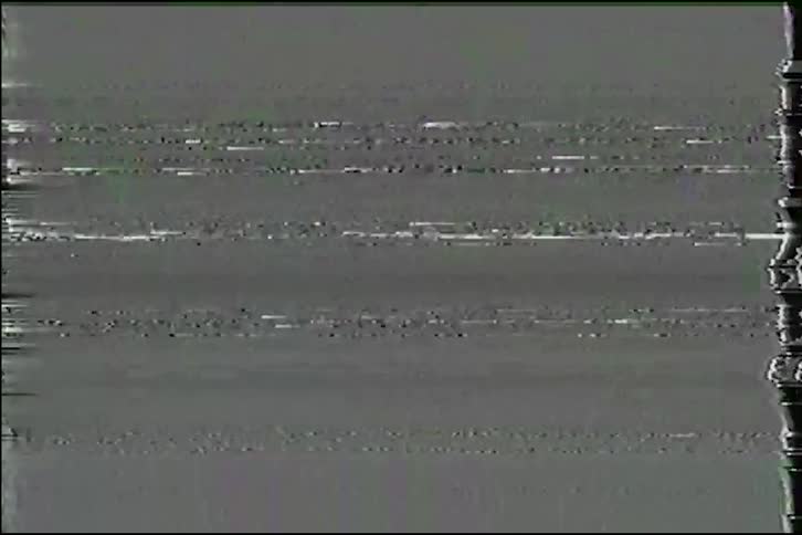 An analog video glitch effect with heavy static, noise, and color distortion reminiscent of a damaged VHS tape