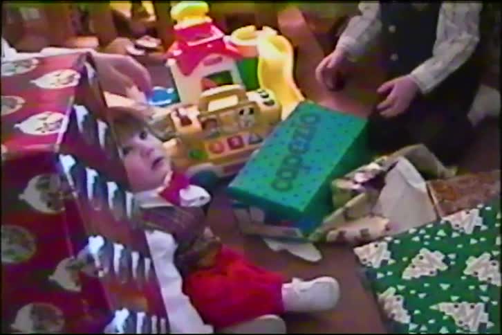 Vintage VHS footage shows a sleepy baby opening Christmas presents with their family