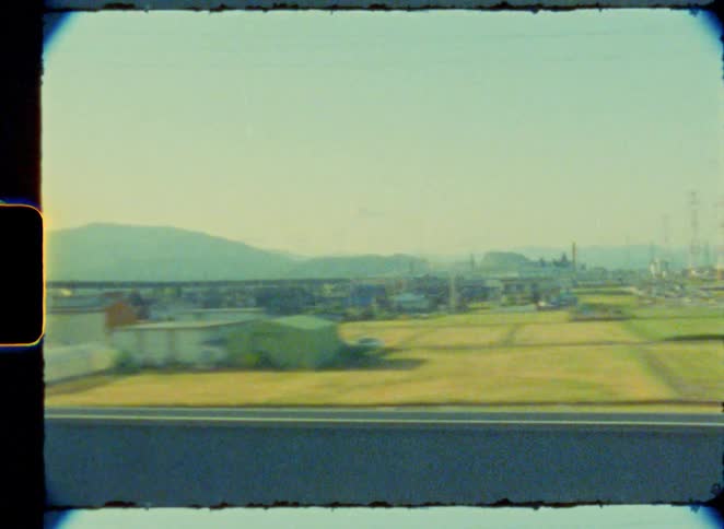 Vintage 8mm film captures the view of the Japanese countryside, with its fields and highways, from a moving train