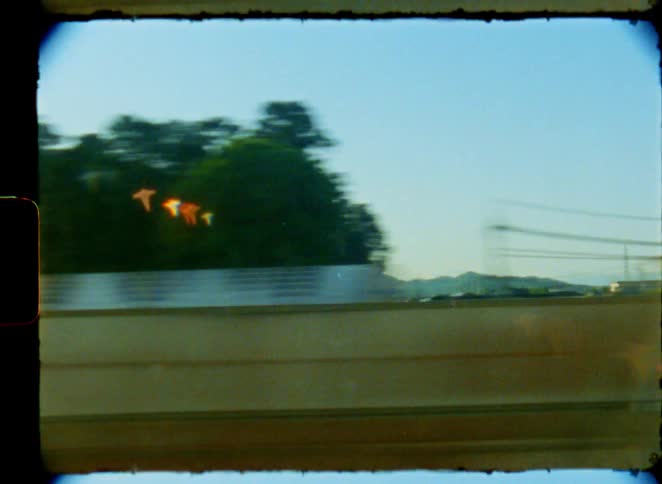 A view from a moving train window reveals the serene Japanese countryside with rice fields and mountains, captured on vintage 8mm film