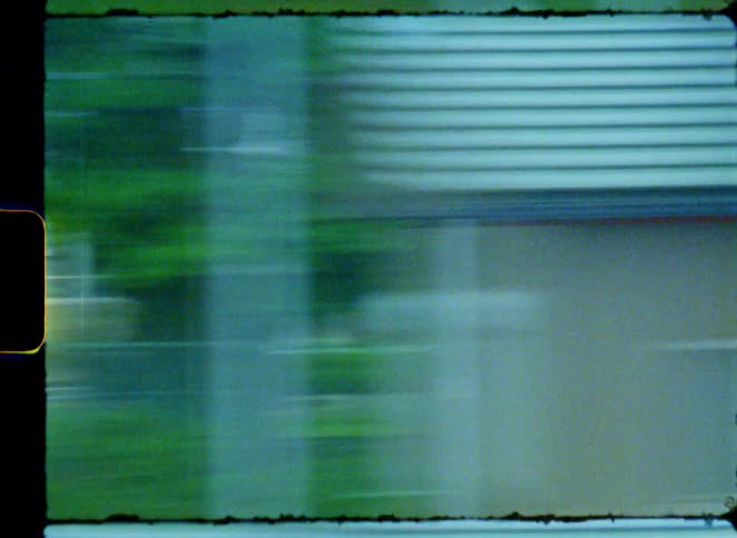 A dreamy, vintage film point-of-view shot from a speeding train passing through a suburban Japanese town with mountains in the background