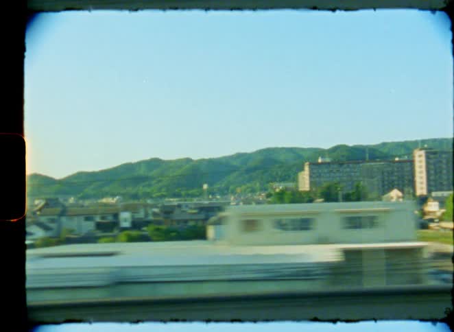 An 8mm film captures views of a Japanese city from a moving train and a man walking down a narrow urban street
