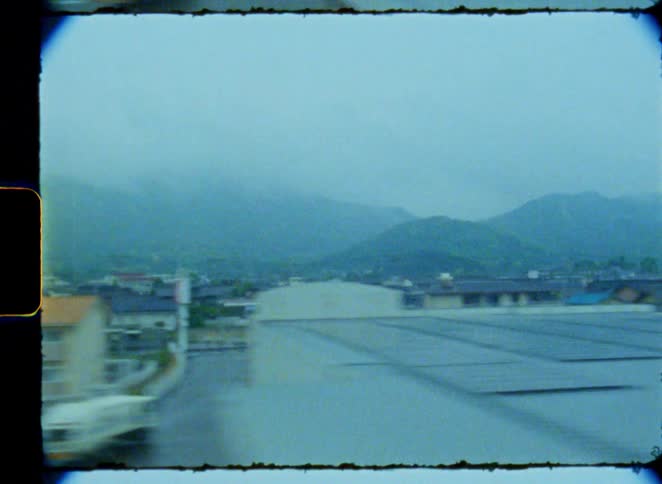 A blurry, nostalgic view of a foggy Japanese town from a moving train, captured on grainy vintage film