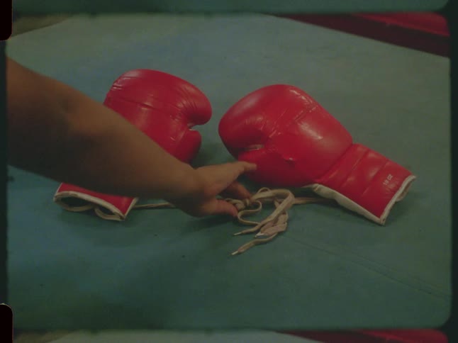 A person removes a pair of red boxing gloves from the canvas of a ring in this vintage-style footage