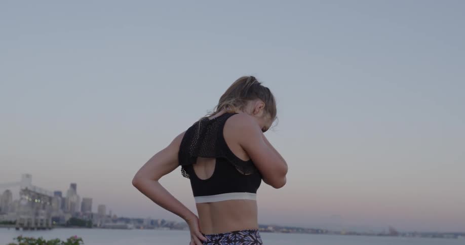 A woman in workout clothing stretches near a lake