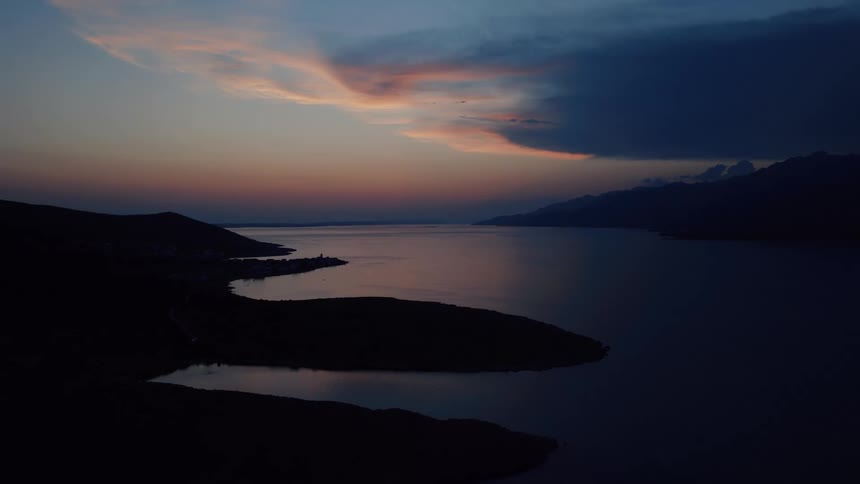 A serene wide shot of a calm sea bay surrounded by silhouetted mountains during the beautiful blue hour after sunset