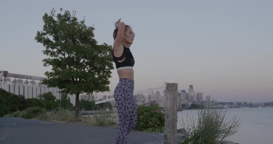 A woman in athletic clothing is standing looking around near a harbor