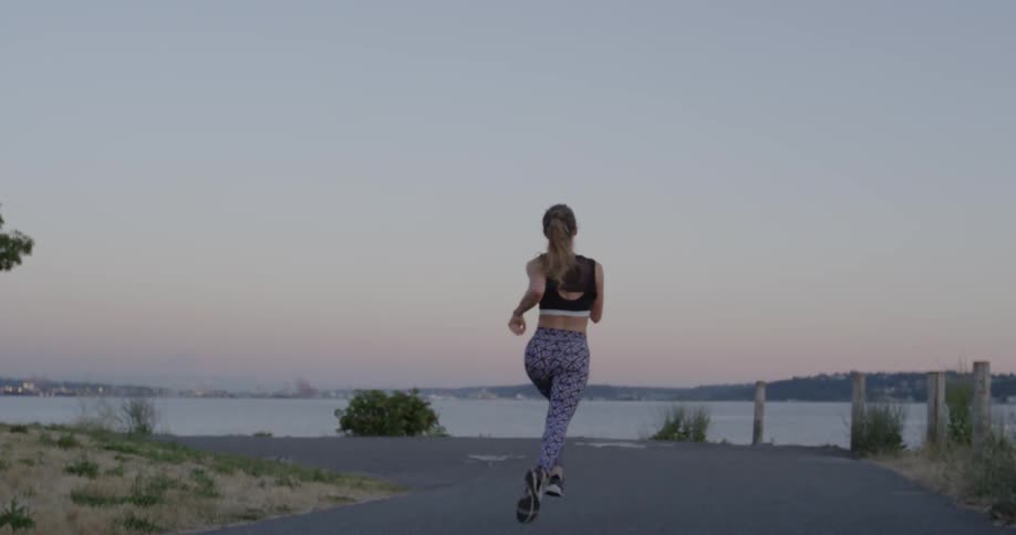 A female jogger is running on a path near a harbor