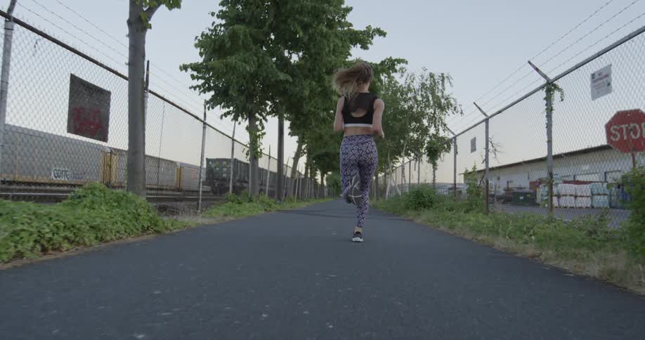 A woman is jogging down a rail near fences