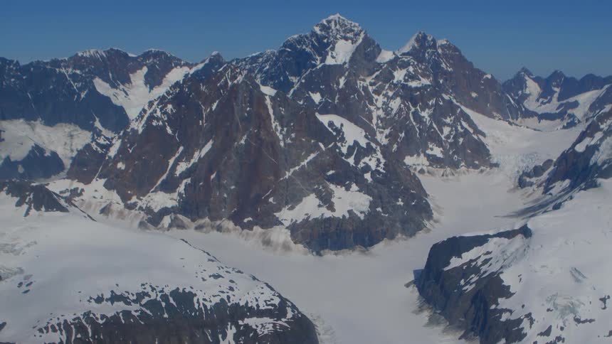 A static, awe-inspiring aerial view of a majestic snow-capped mountain range and its vast glaciers under a clear blue sky