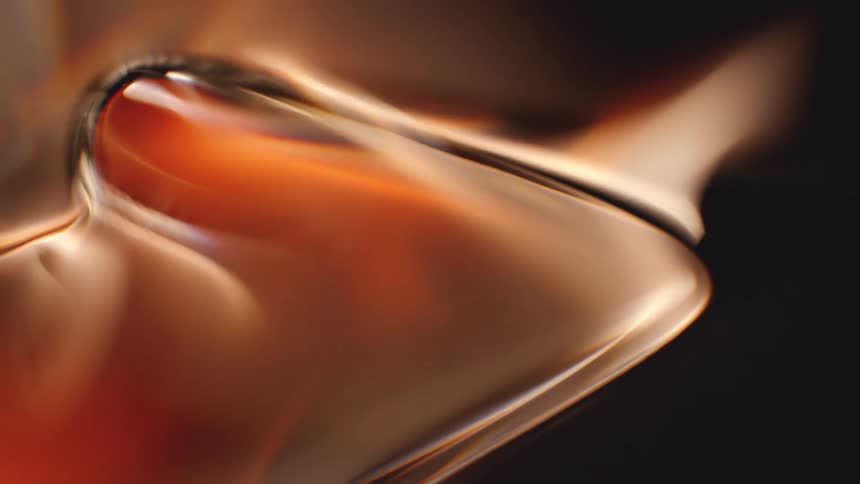 An extreme close-up of a viscous, amber-colored liquid slowly flowing and shifting against a dark background