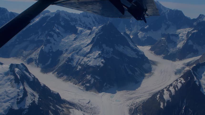 A stunning aerial view from an airplane flying over a vast, majestic mountain range covered in snow and glaciers
