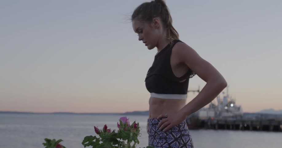 A woman in a sports bra catches her breath while standing by a lake at sunset
