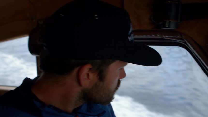 Slow motion profile of a bearded man in a cap looking out a boat window at the churning ocean wake