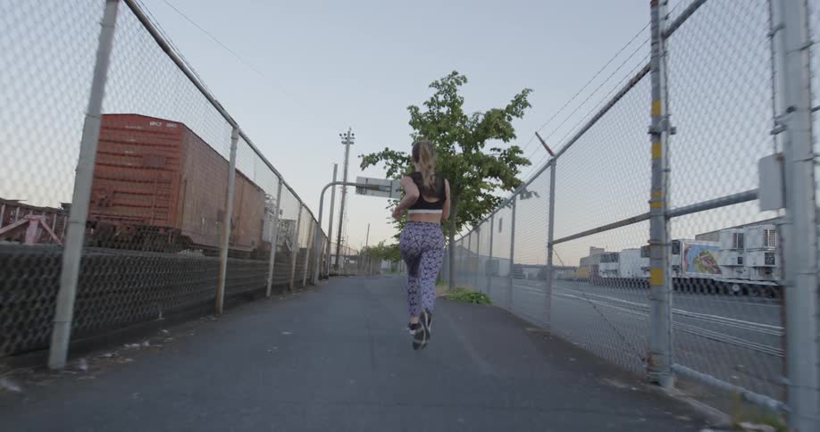 A female jogger is running on a fenced in path near train cars