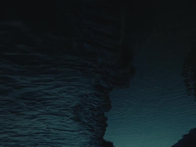 The dark, ethereal reflection of a person and a cliff face ripples in moody, dark green water