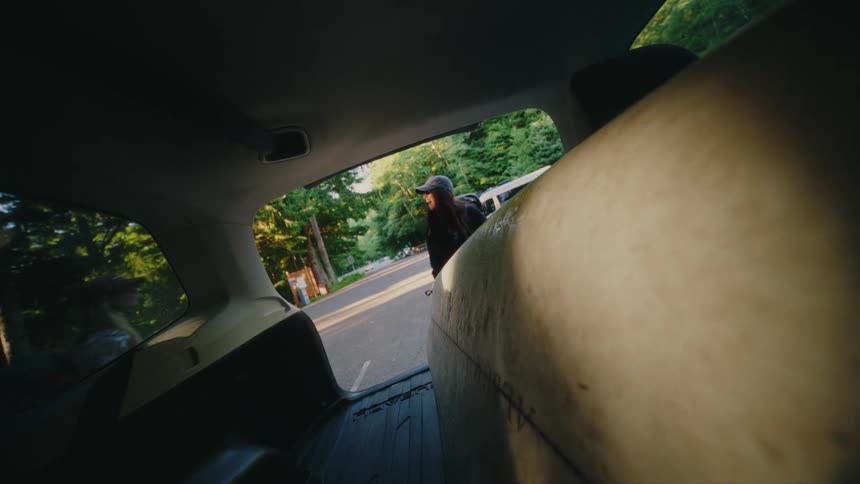 From inside the car, a woman opens the trunk to let her dog out before meeting her friend to go surfing