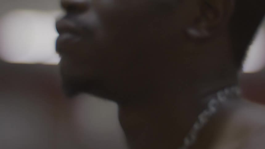 Close-up profile shot of a young Black man dancing in a dark room with soft lighting