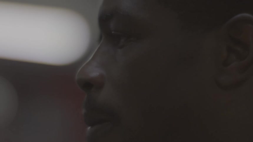 Dramatic close-up profile shot of a serious young Black man in a dimly lit, moody setting as a single braid falls into view