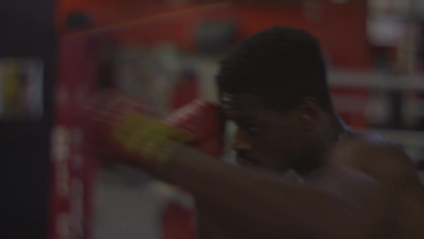 Slow motion close-up of a focused male boxer training on a heavy bag in a dimly lit boxing gym