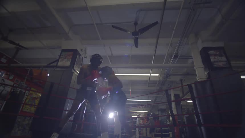 A dramatic low-angle shot shows two boxers sparring intensely inside a boxing ring