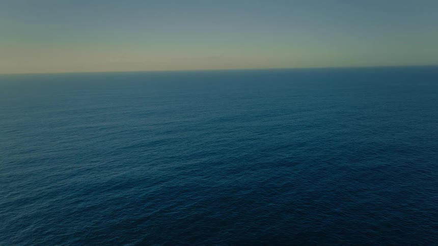 A serene aerial view of the deep blue open ocean stretching to the horizon under a clear twilight sky
