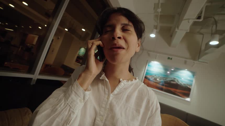 A smiling woman talks on her smartphone in a modern office space late at night as the camera slowly pushes in on her