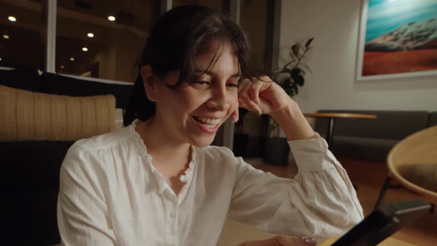 A smiling woman enjoys watching content on her smartphone in a cozy, modern living room at night