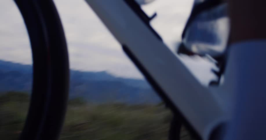 Cinematic low-angle close-up of a cyclist's feet pedaling a bicycle on a gravel path in slow motion at dusk