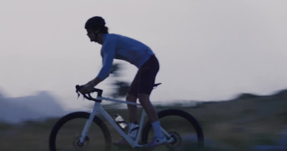 Slow motion side view of a cyclist riding a gravel bike on a scenic mountain trail at dusk
