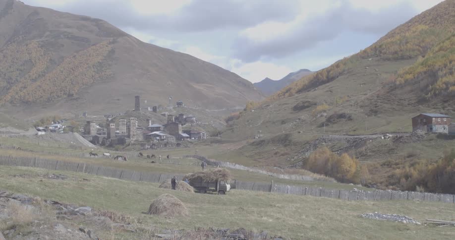 Farmers gather hay in a field overlooking the ancient stone Svaneti towers of a remote mountain village in Georgia