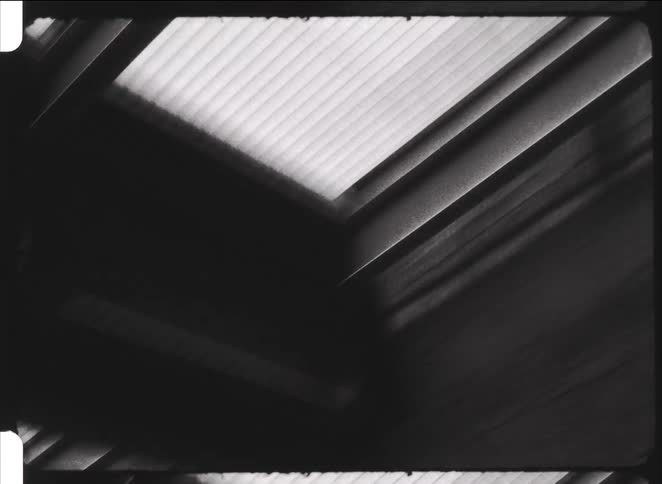A chaotic and abstract black and white handheld shot looks up at industrial ceiling lights, creating a dizzying effect
