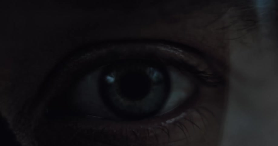 An intense macro shot captures a person's eye slowly opening in the dark