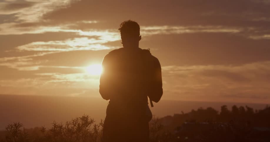 Silhouette of a hiker with a backpack watching the golden sunset over the ocean from a scenic lookout