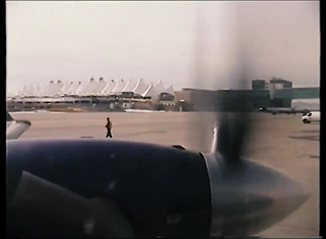 Archival footage from a propeller plane window captures the spinning propeller on the tarmac at Denver International Airport