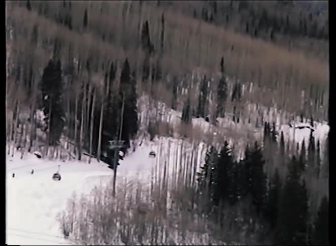 A vintage panning shot captures skiers and gondolas moving across a vast snowy mountain landscape at a ski resort