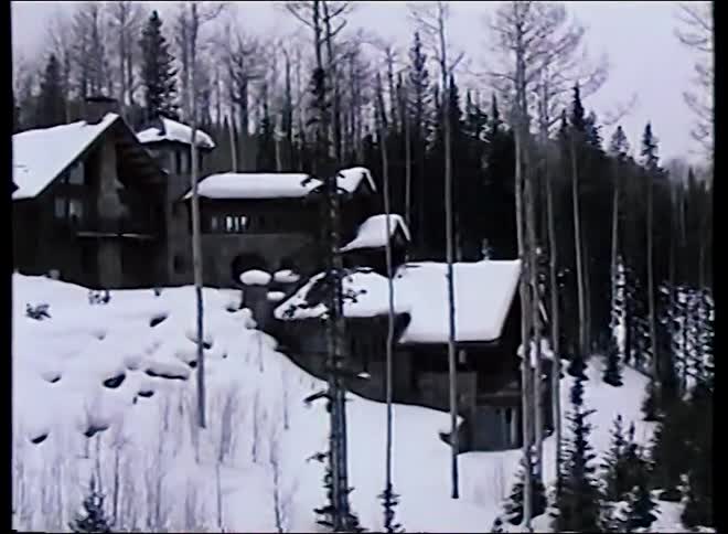 Vintage footage from a ski lift reveals a beautiful, snow-covered lodge nestled in a dense forest of aspen and pine trees