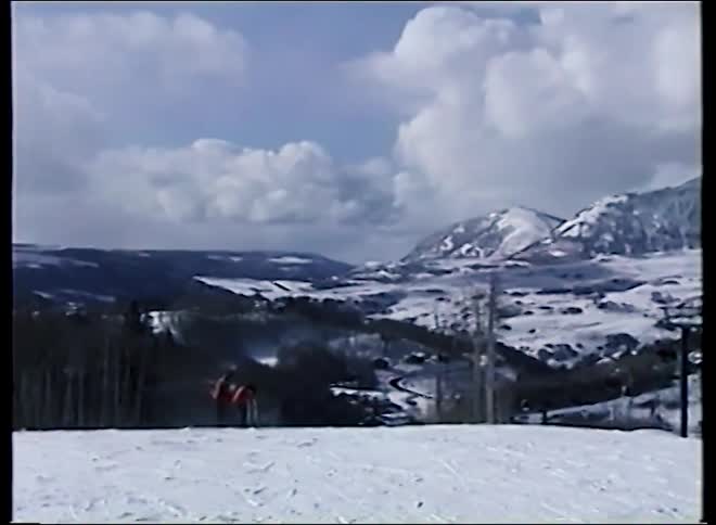 Vintage footage pans across a vast snowy mountain landscape at a ski resort with active chairlifts and skiers