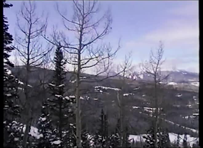 A vintage, panning shot reveals a majestic snow-covered mountain range and ski resort on a winter day