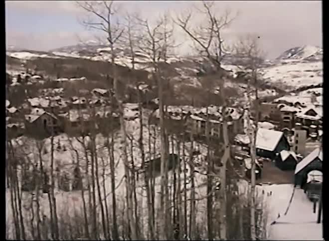 Vintage 1990s footage offers a scenic view from a ski lift overlooking a snowy mountain resort and village below