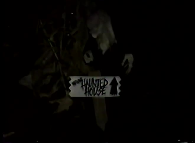 Spooky vintage VHS footage reveals a monster next to a sign pointing to a haunted house at night