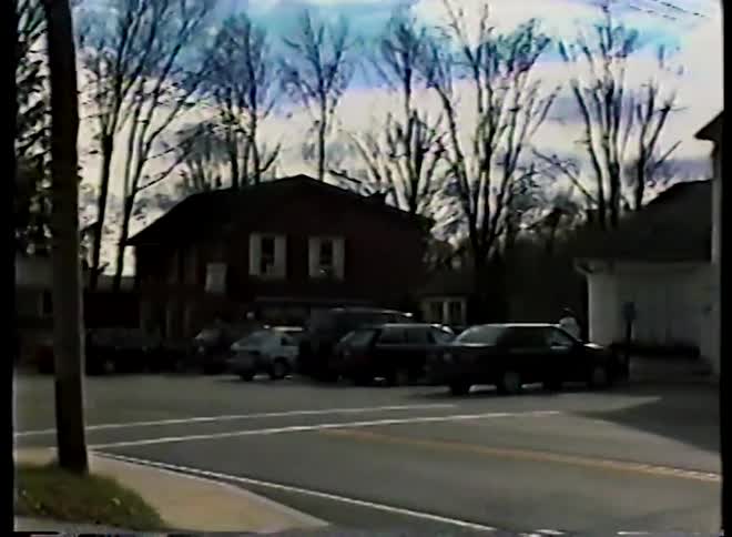 Vintage VHS footage pans across a quiet street in a small American town with classic architecture and parked cars