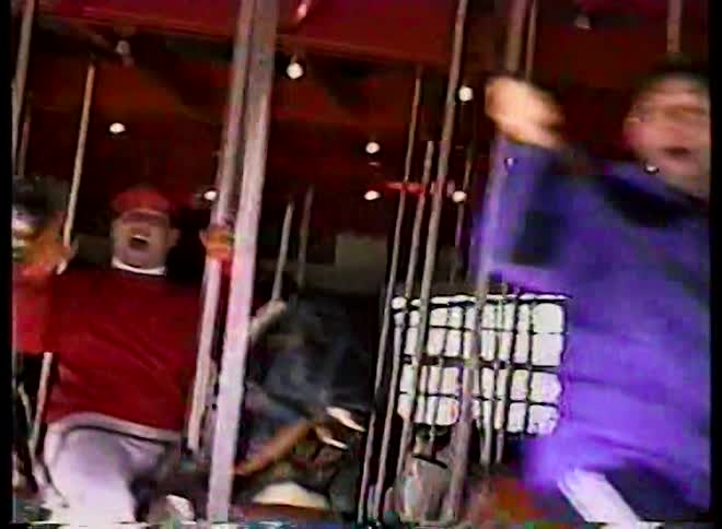 Excited adults and children shout with joy while riding on a spinning carousel in this vintage home video