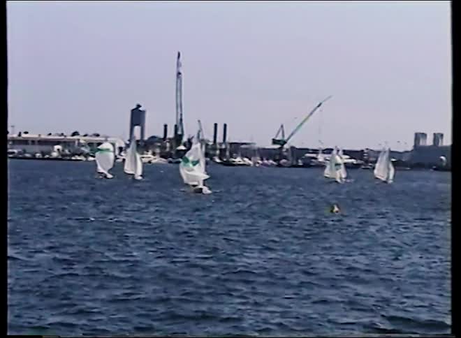 Vintage 1989 footage shows a fleet of sailboats with spinnakers up during a race in an industrial harbor