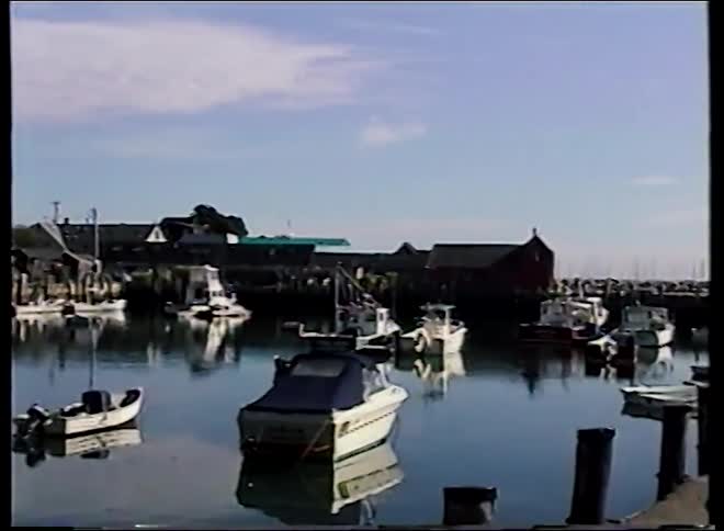 Vintage VHS footage pans across a picturesque New England harbor in Rockport, Massachusetts, showing boats reflecting in the calm water
