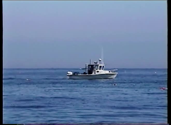 Vintage footage slowly zooms in on a small white fishing boat floating peacefully on the vast blue ocean