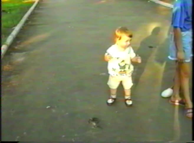 A cute toddler joyfully takes wobbly first steps on a sidewalk in this heartwarming vintage home video