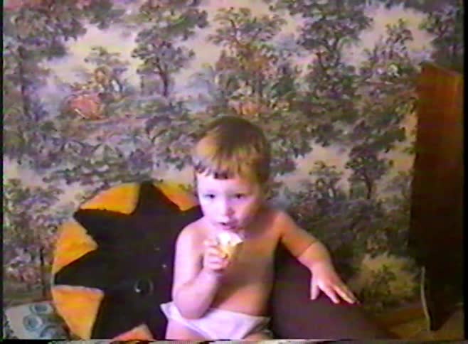 A vintage VHS home video captures a cute toddler in a diaper eating an ice cream cone in a retro room