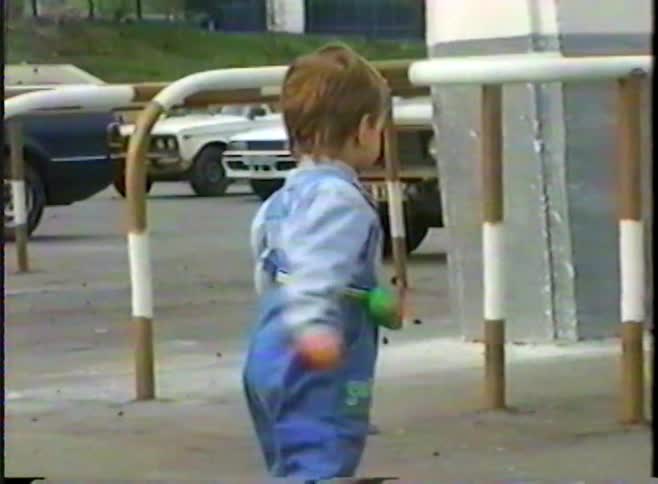Nostalgic home video footage captures a joyful toddler in denim overalls walking and smiling in a parking lot